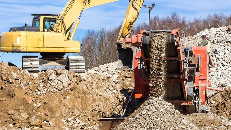 A yellow excavator and a red machine are working at an excavation site.