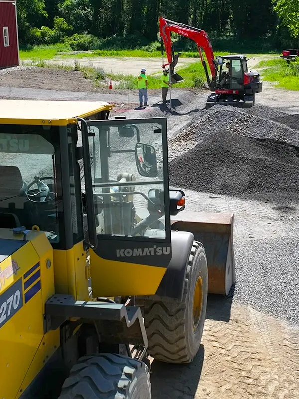 A yellow excavator is parked near a construction site with two men standing nearby.