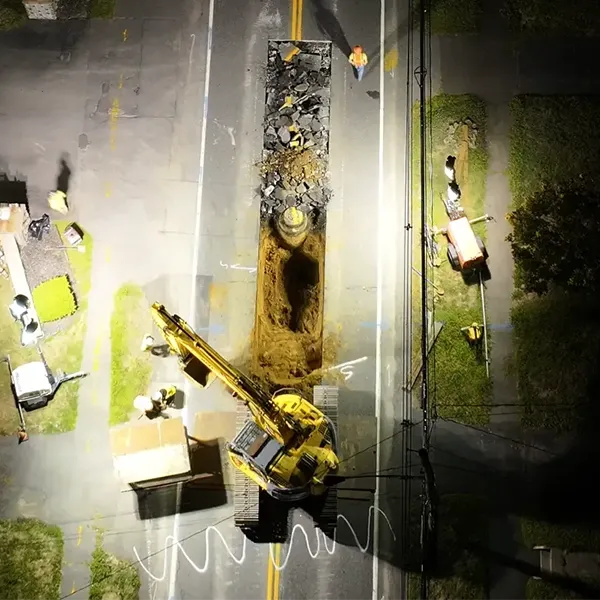 A construction site with vehicles and equipment is surrounded by trees at night.