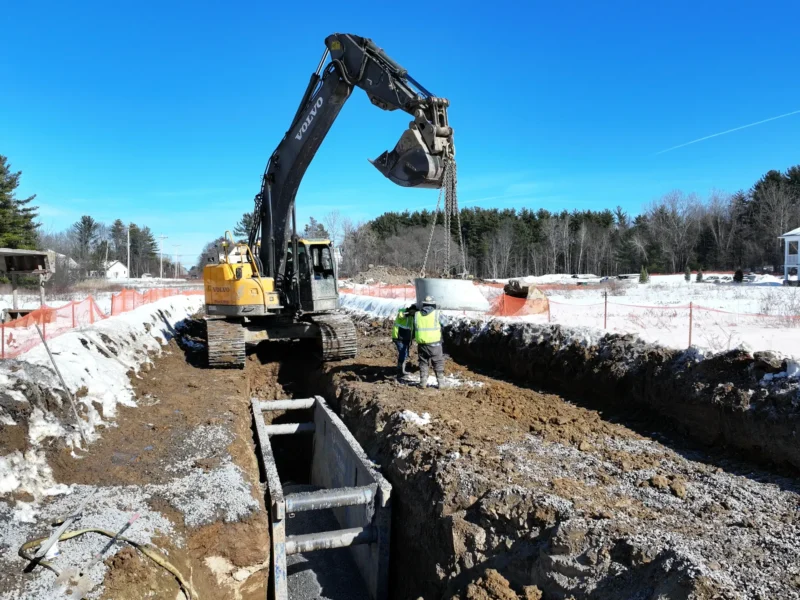 An excavator is digging a hole with an operator nearby.