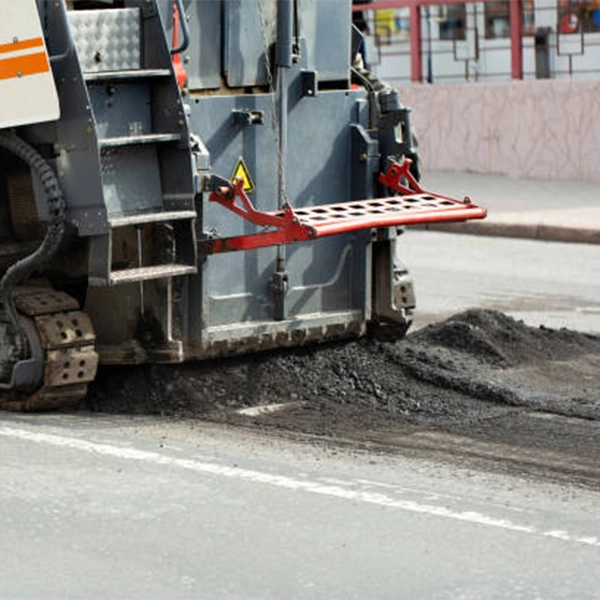 An asphalt reclamation machine is driving down a road and crushing up asphalt.