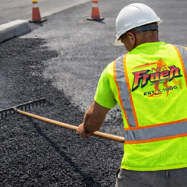 A construction worker is raking asphalt on a road.